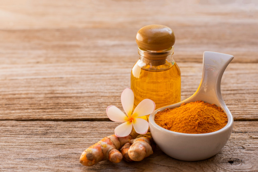 Turmeric powder in white ceramic bowl with turmeric roots and glass bottle of turmeric oil on rustic wooden table, natural herbal remedy concept