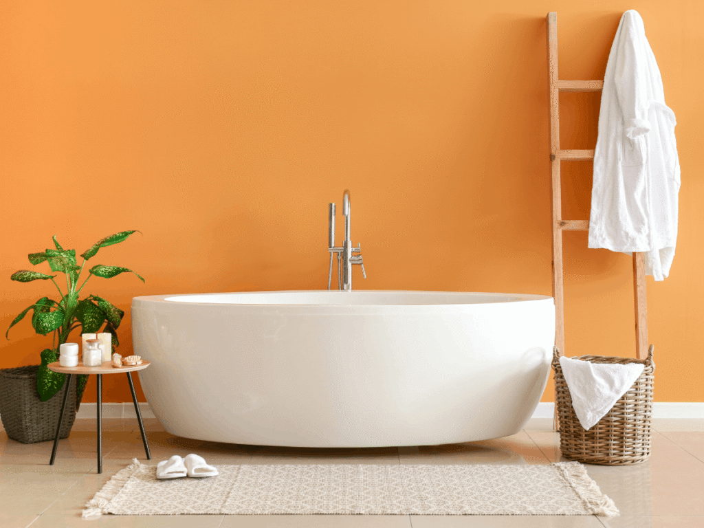 Modern bathroom with fiberglass freestanding bathtub, orange accent wall, wood ladder, and decor creating a bright, stylish, spa-like space.