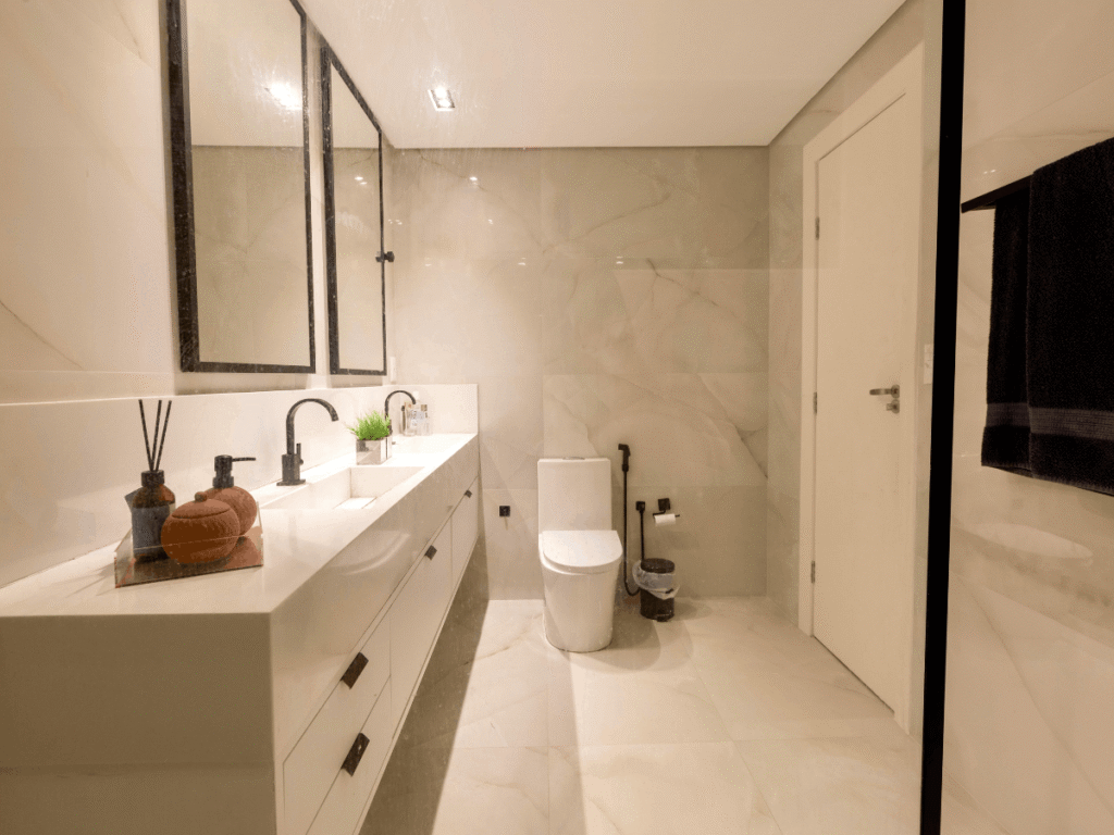 Spacious beige bathroom with marble tile walls, double vanity, black fixtures, large mirrors, and modern toilet in a clean, minimalist design.