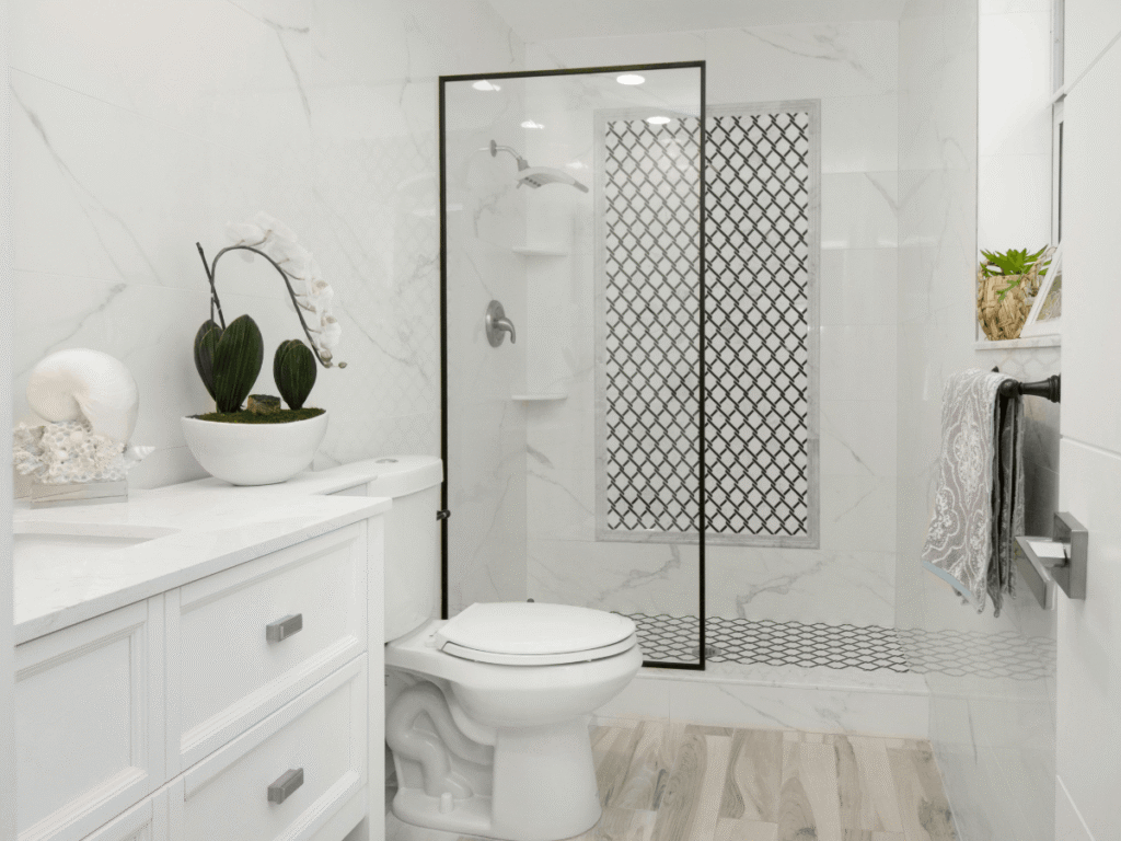 Bright white bathroom with marble tile walls, glass walk-in shower with black frame, white vanity, and modern fixtures creating a clean, elegant look.